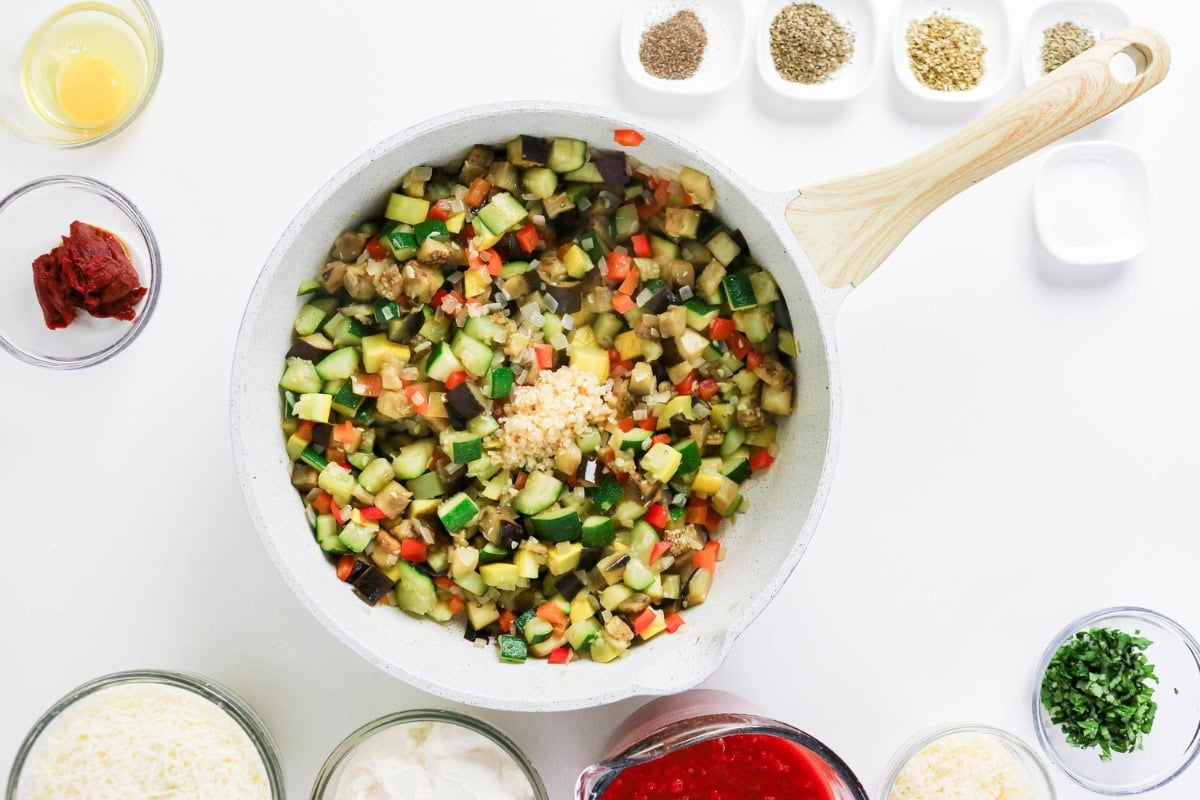 Chopped vegetables cooking in a white pan, surrounded by seasonings and sauces.