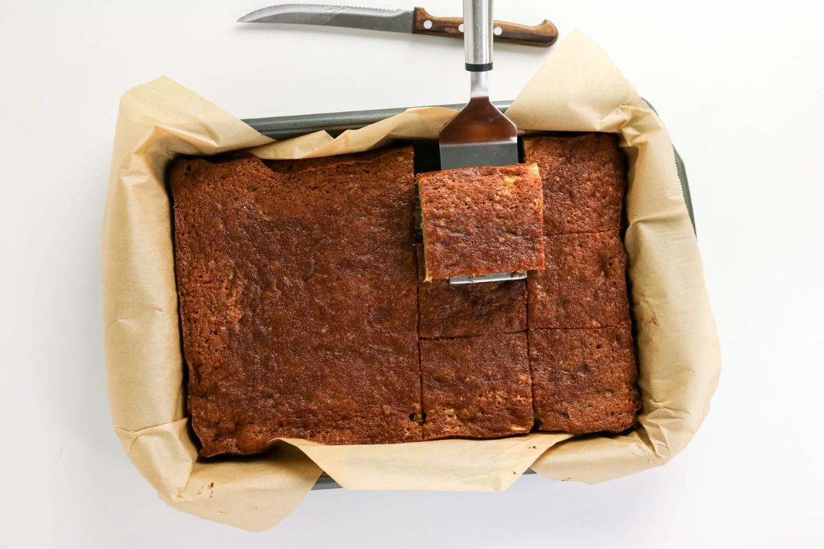 A spatula lifts a square of brownies from a parchment-lined baking pan.
