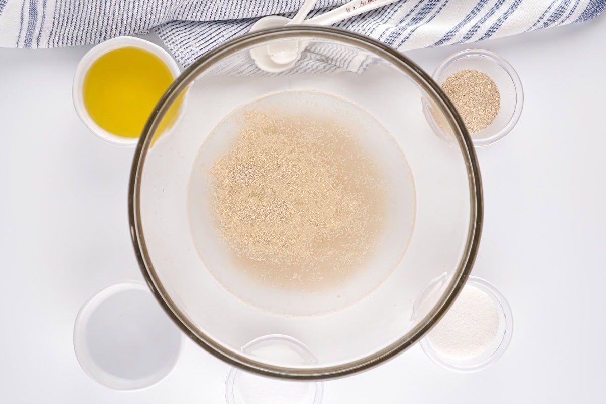 A bowl with yeast mixture, surrounded by small bowls of ingredients.