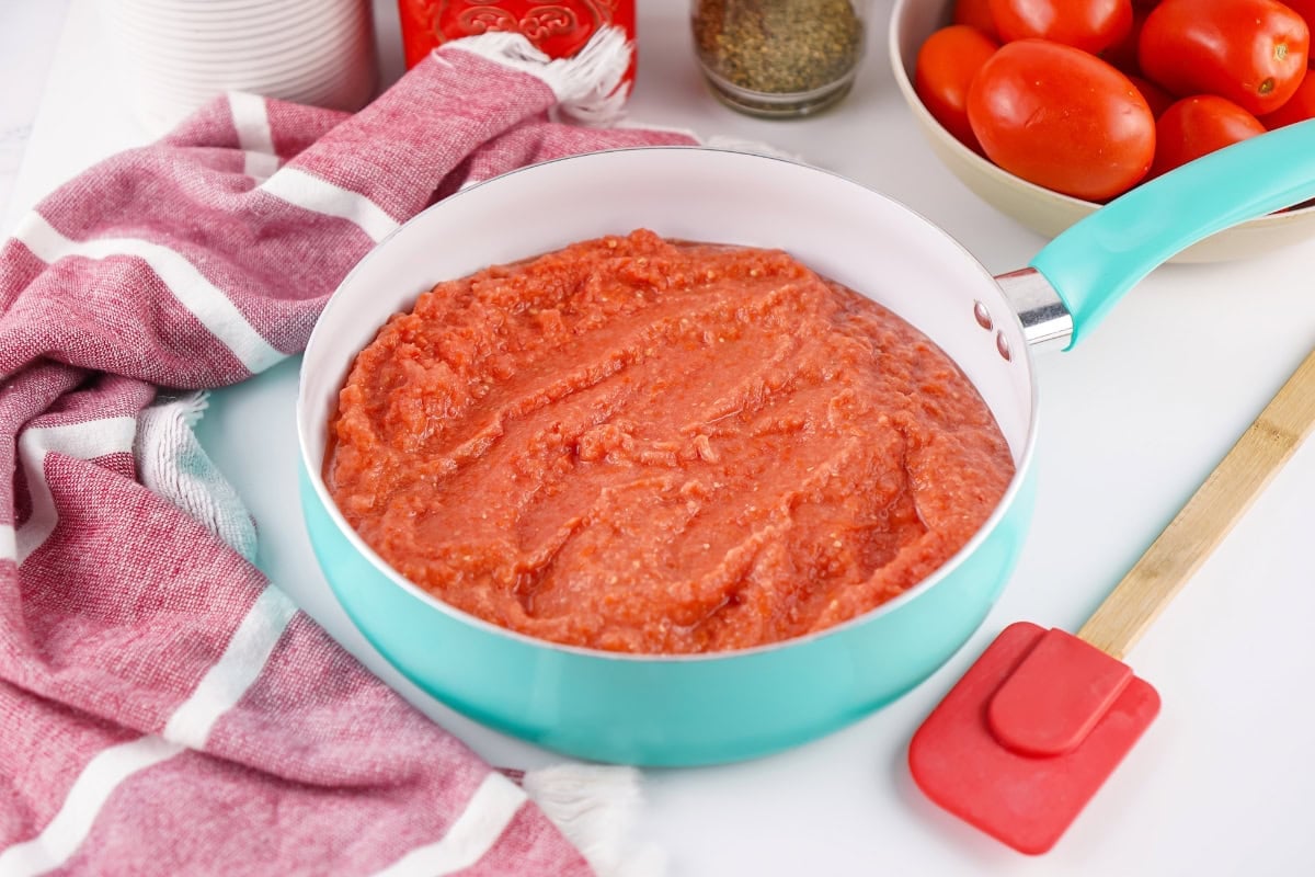 Aqua pan with tomato sauce next to a red spatula and fresh tomatoes.