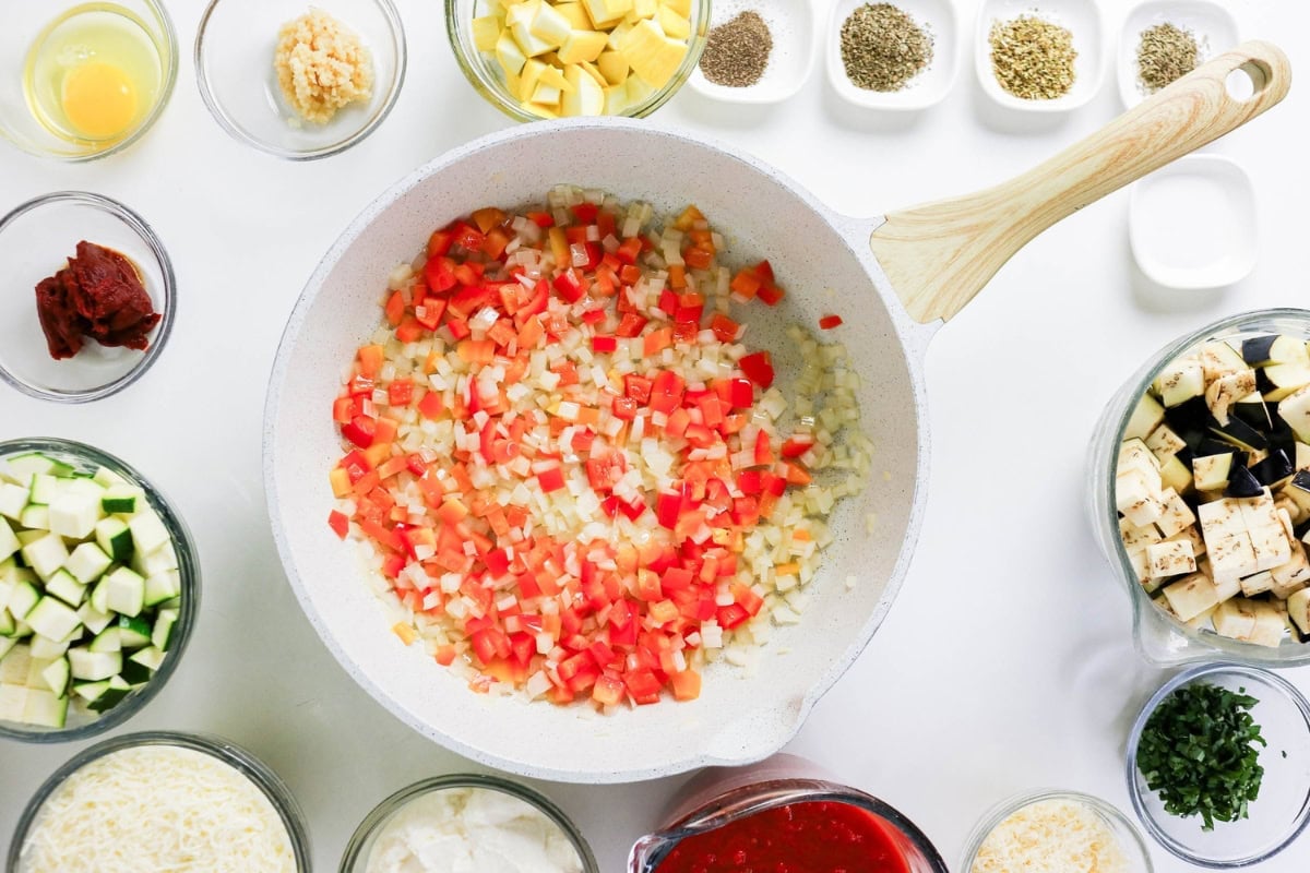 Chopped vegetables cooking in a white pan, surrounded by various ingredients.