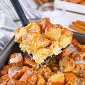 A spatula lifts a glazed bread pudding from a baking pan.
