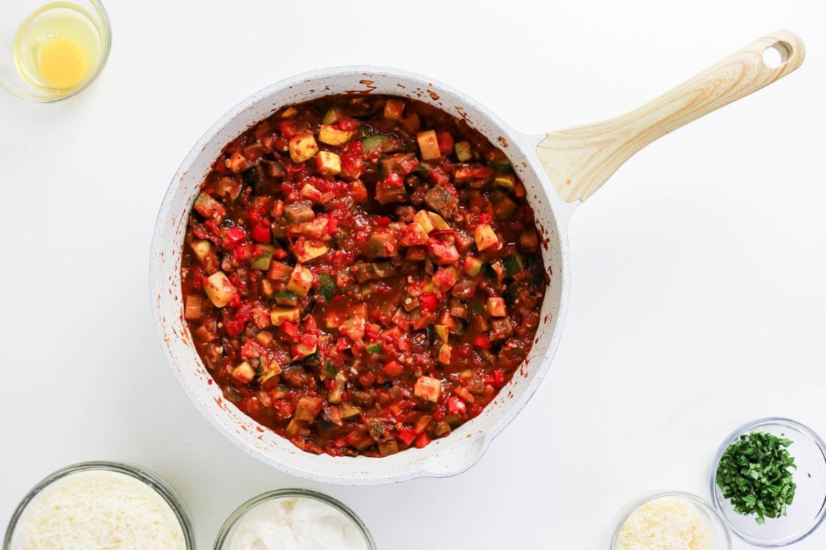 A pot of vegetable stew with bowls of oil, cheese, and herbs are on the side.
