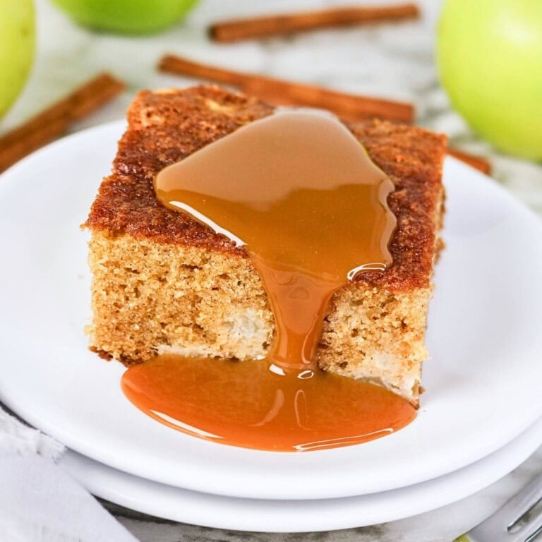 A slice of cake with caramel sauce on top, served on a white plate.