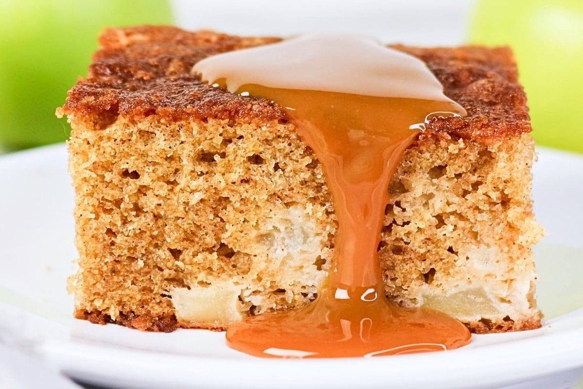 A slice of apple cake topped with caramel sauce on a white plate.