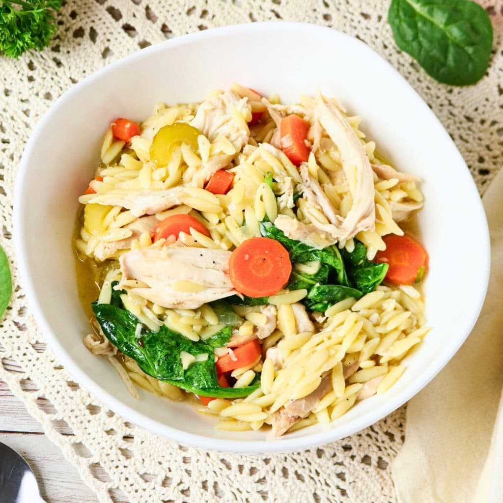 Bowl of orzo pasta with shredded chicken, spinach, and sliced carrots.