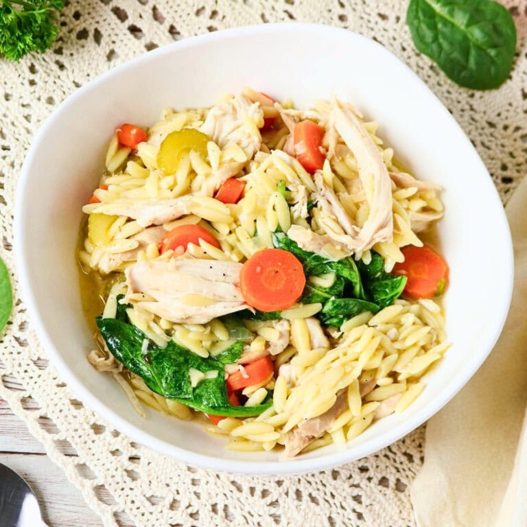 Bowl of orzo pasta with shredded chicken, spinach, and sliced carrots.