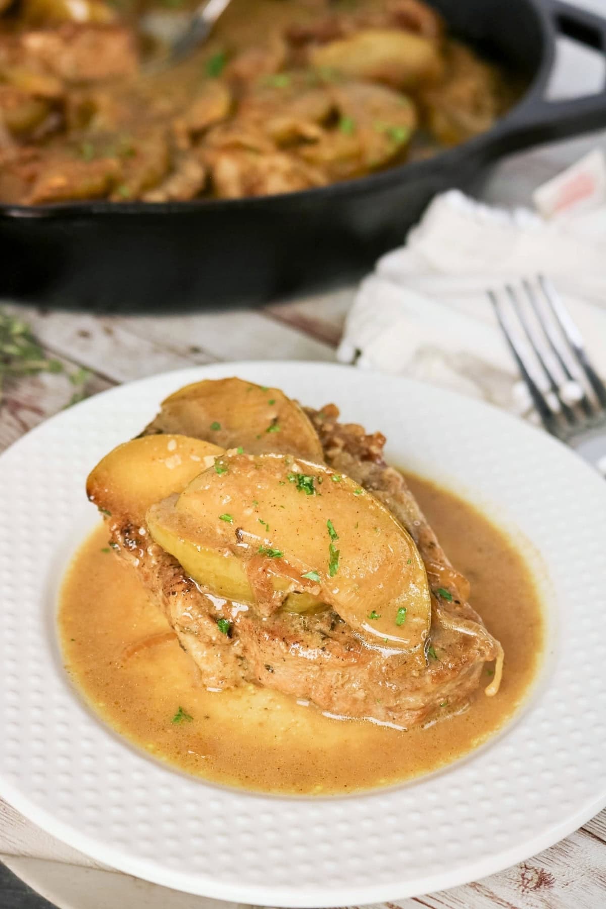 Pork chop with apples and sauce on a white plate.