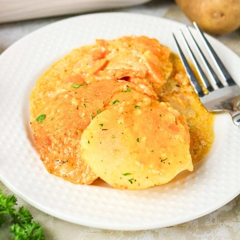 Three cheesy scalloped potatoes on a white plate with a fork beside them.