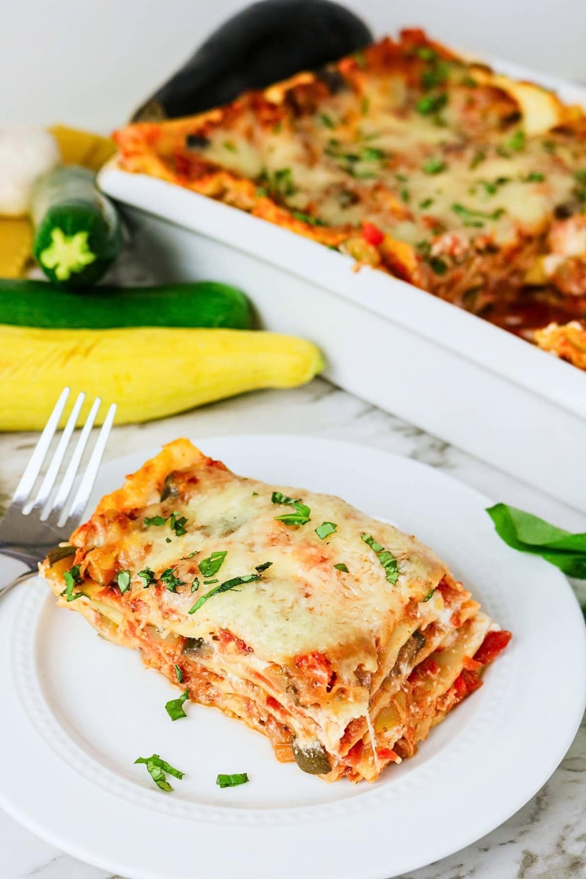 A slice of vegetable lasagna on a plate, with the casserole in the background.