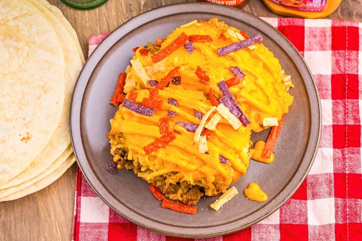 Cheesy taco-filled tortillas on a plate with red and purple tortilla strips.