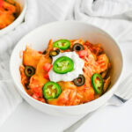 Bowl of cheesy chicken topped with jalapenos, olives, tomatoes, and sour cream.
