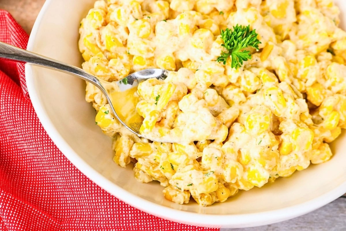 Creamy corn salad in a bowl with a spoon and parsley garnish.
