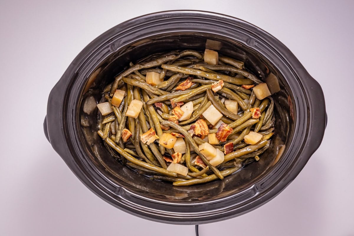 Green beans, potatoes, and bacon pieces in a slow cooker.