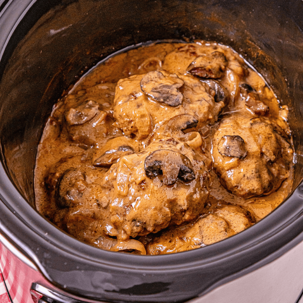 Beef patties with mushroom gravy cooking in a slow cooker.