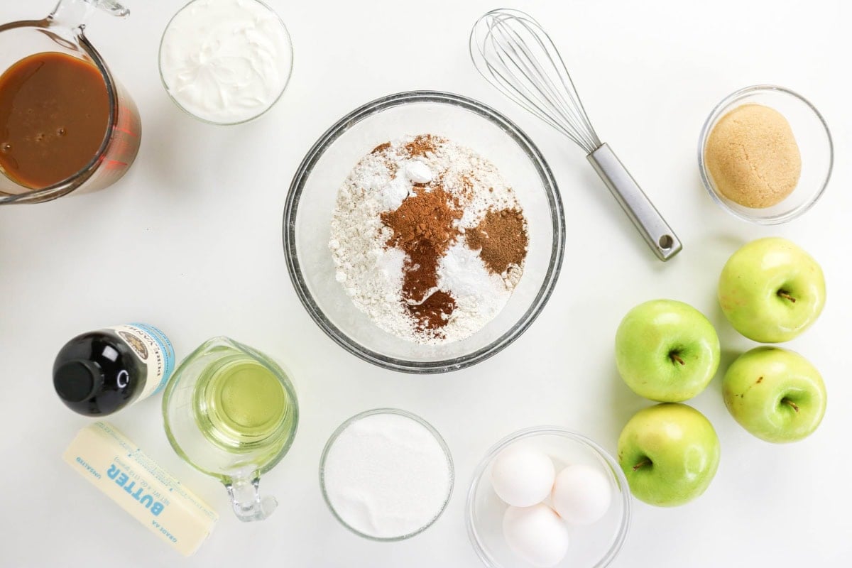 Baking ingredients and green apples arranged on a white surface.