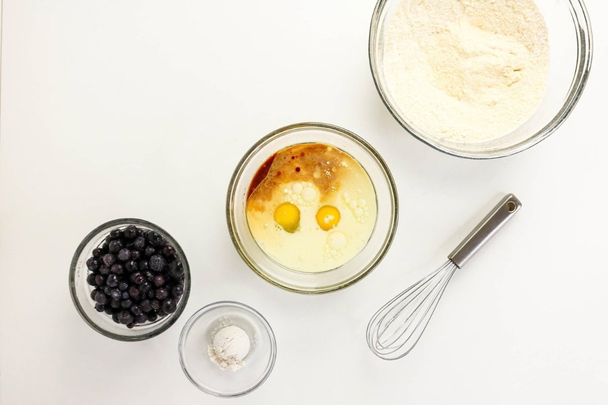 Baking ingredients and a whisk arranged on a white surface.