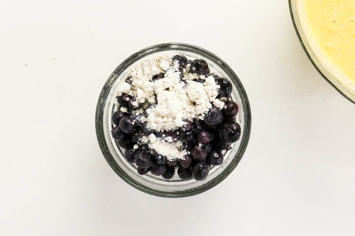 Glass bowl with blueberries topped with flour, viewed from above.