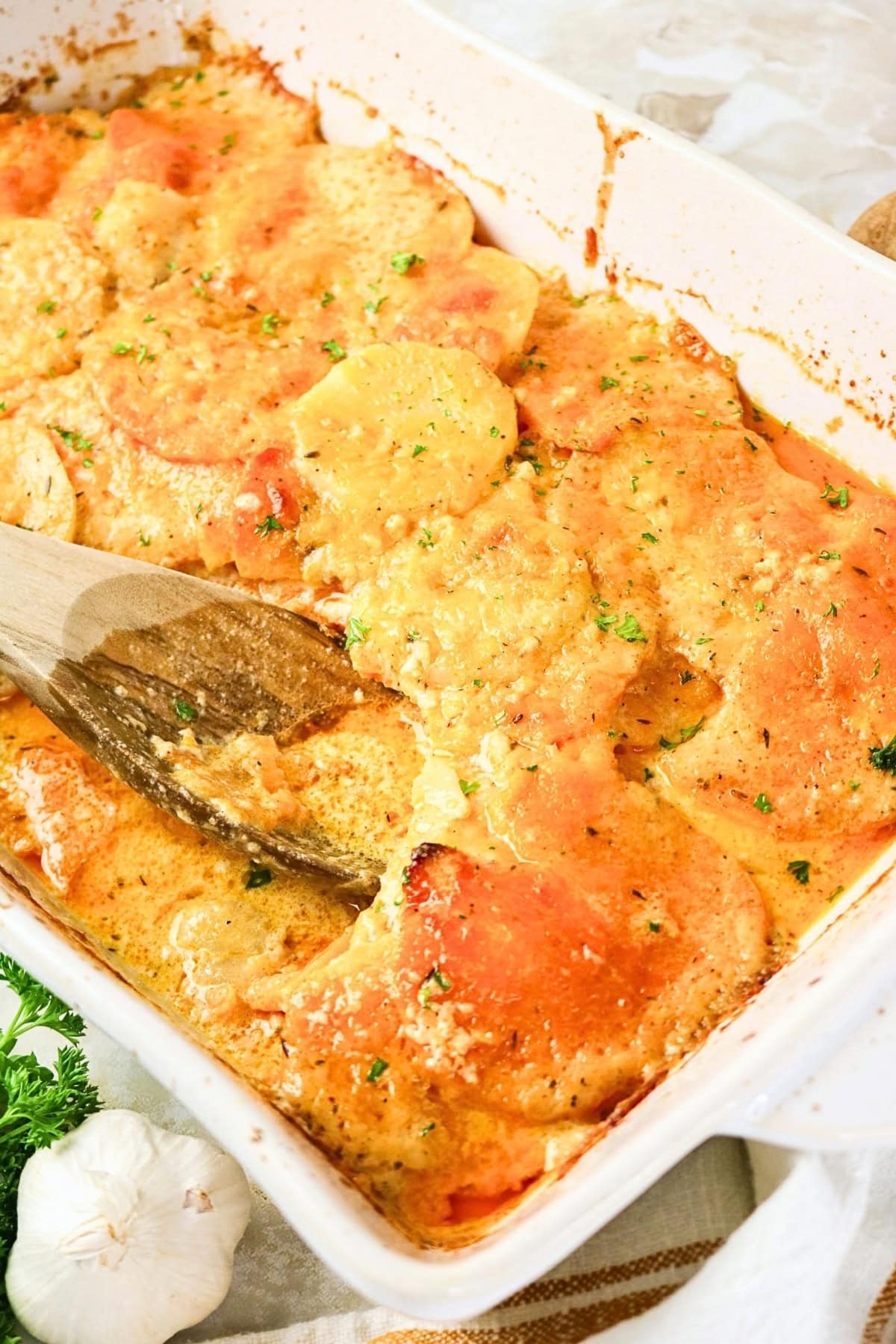 Golden cheesy scalloped potatoes in a white baking dish with a wooden spoon.
