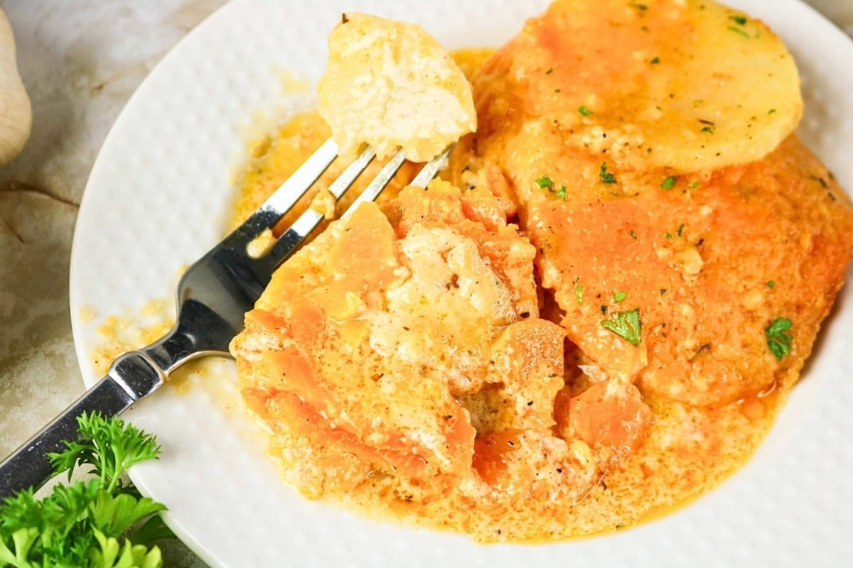 Sliced cheesy potatoes on a white plate with a fork and creamy sauce.