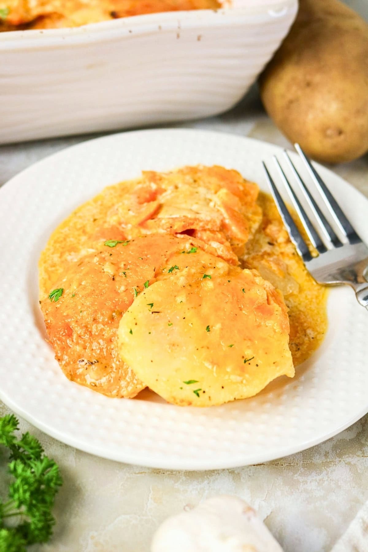 Scalloped potatoes with cheese sauce served on a white plate with a fork.