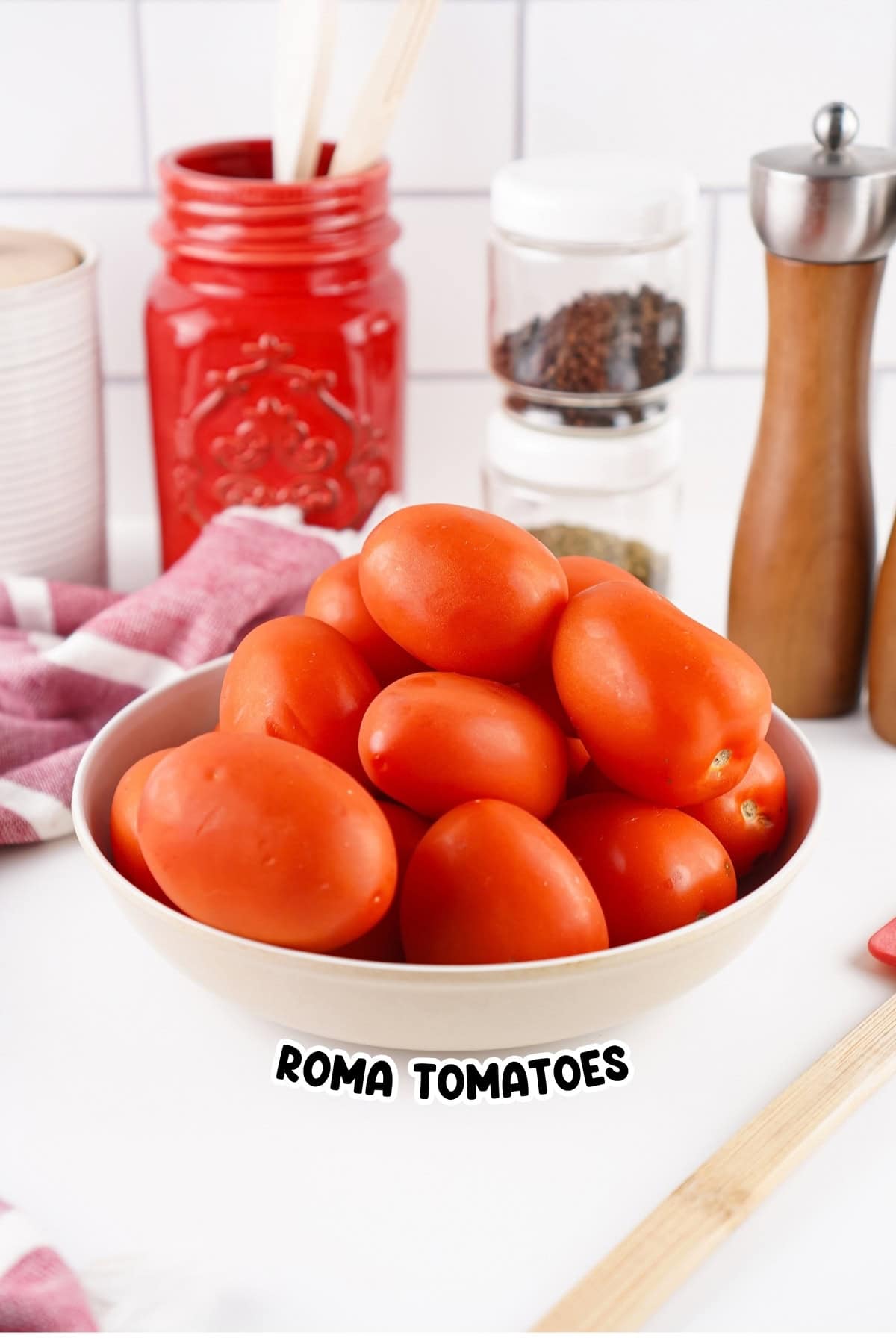A bowl of Roma tomatoes on a kitchen counter with various utensils behind.