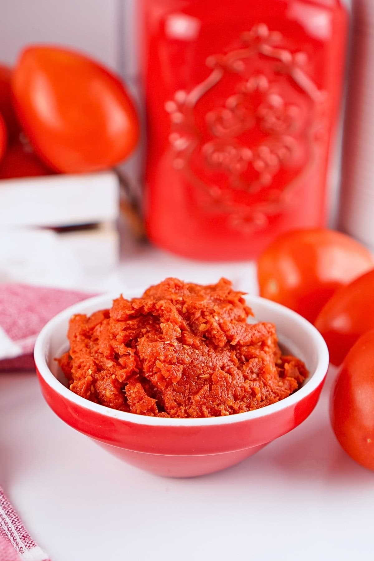 A bowl of red tomato paste surrounded by fresh tomatoes and red decor.