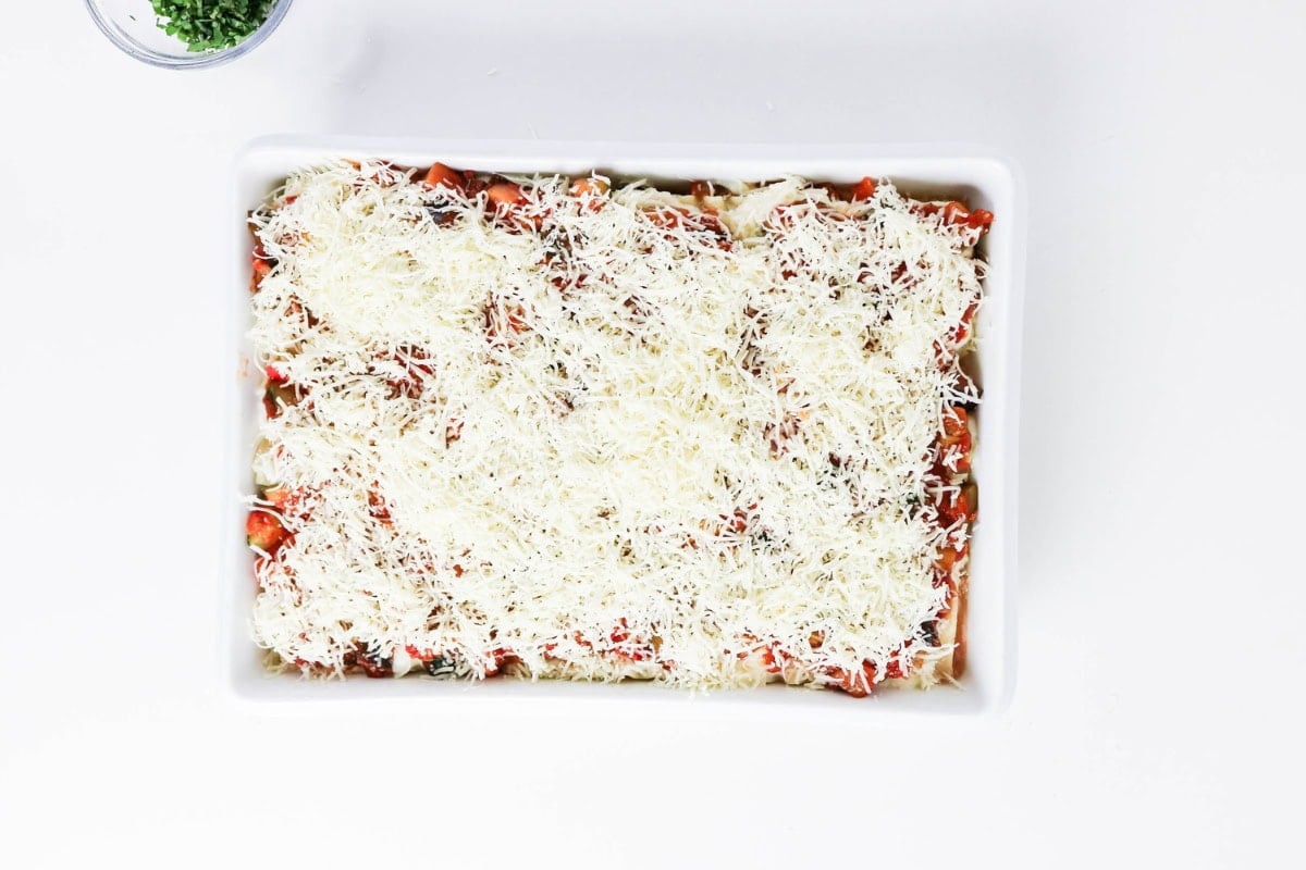 A baking dish with lasagna topped with shredded cheese, ready to bake.