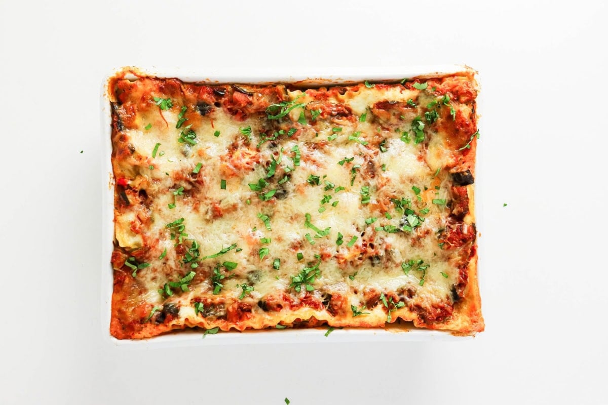 Baked lasagna topped with melted cheese and chopped herbs in a white dish.