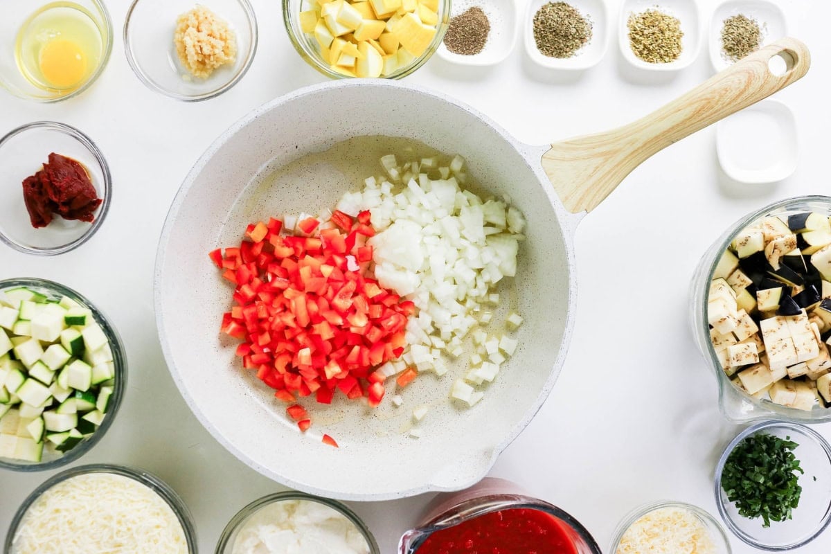 Chopped onions and tomatoes in a pan, surrounded by bowls of ingredients.