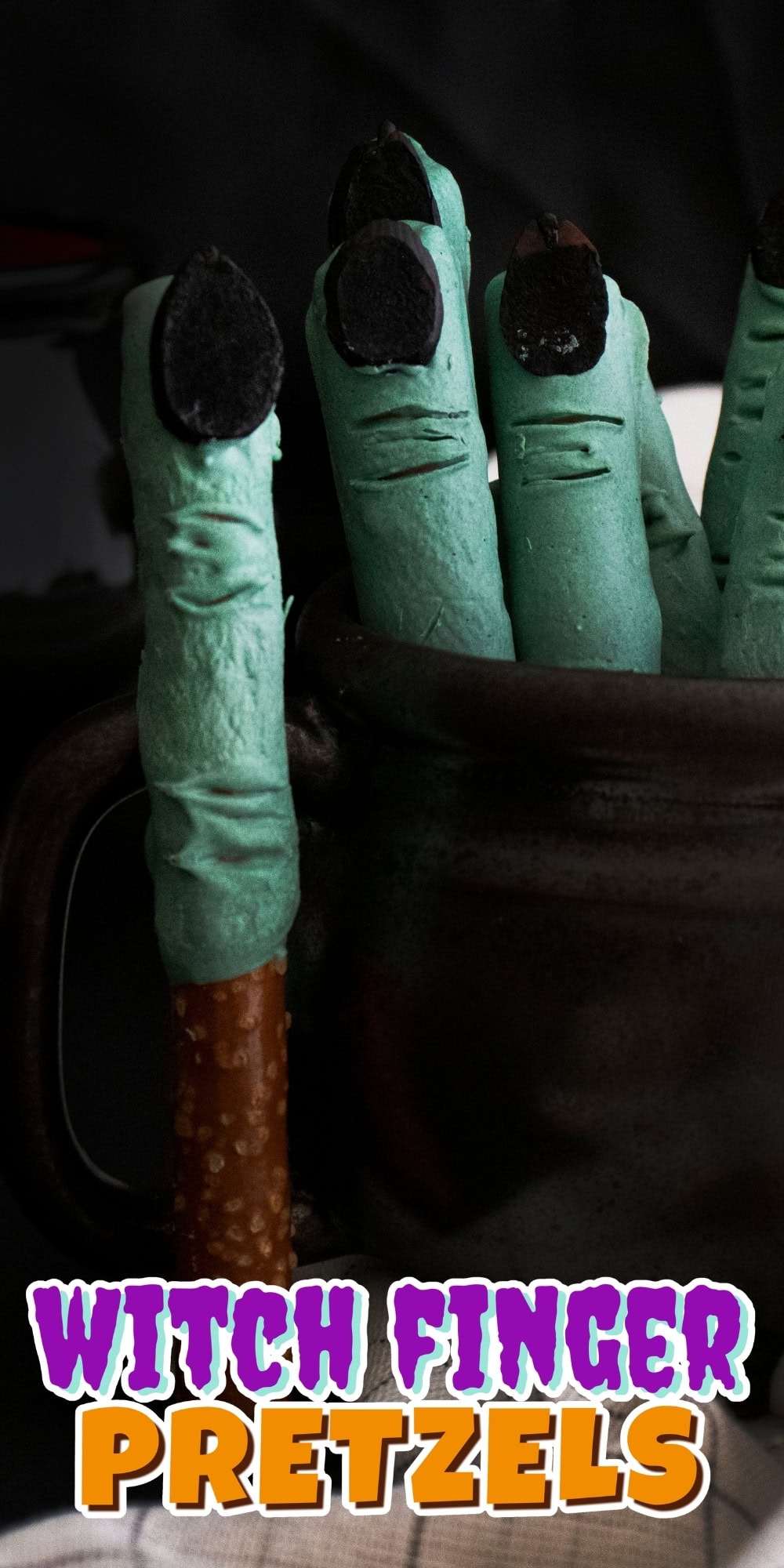 Green witch finger pretzels with black nails in a dark mug.