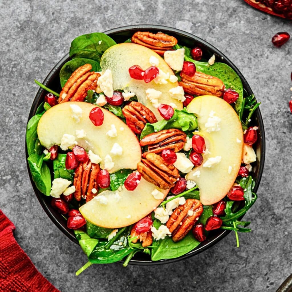 Salad with apple slices, pecans, pomegranate seeds, and crumbled cheese.