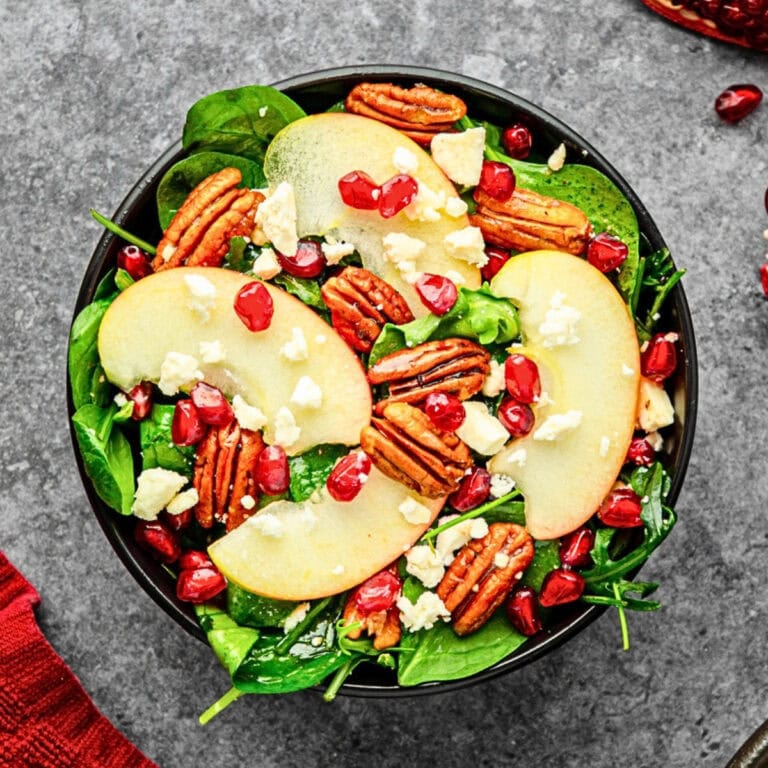 Salad with apple slices, pecans, pomegranate seeds, and crumbled cheese.