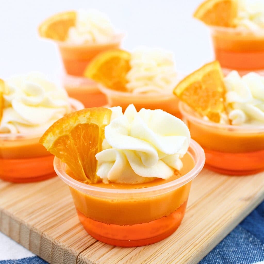 Small orange gelatin cups topped with whipped cream and orange slices.