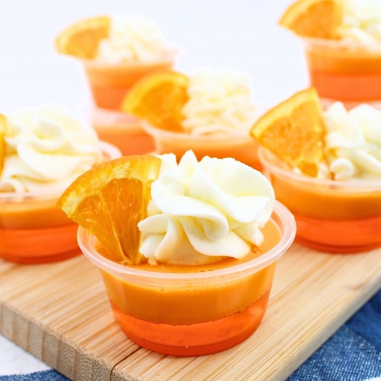 Small orange gelatin cups topped with whipped cream and orange slices.
