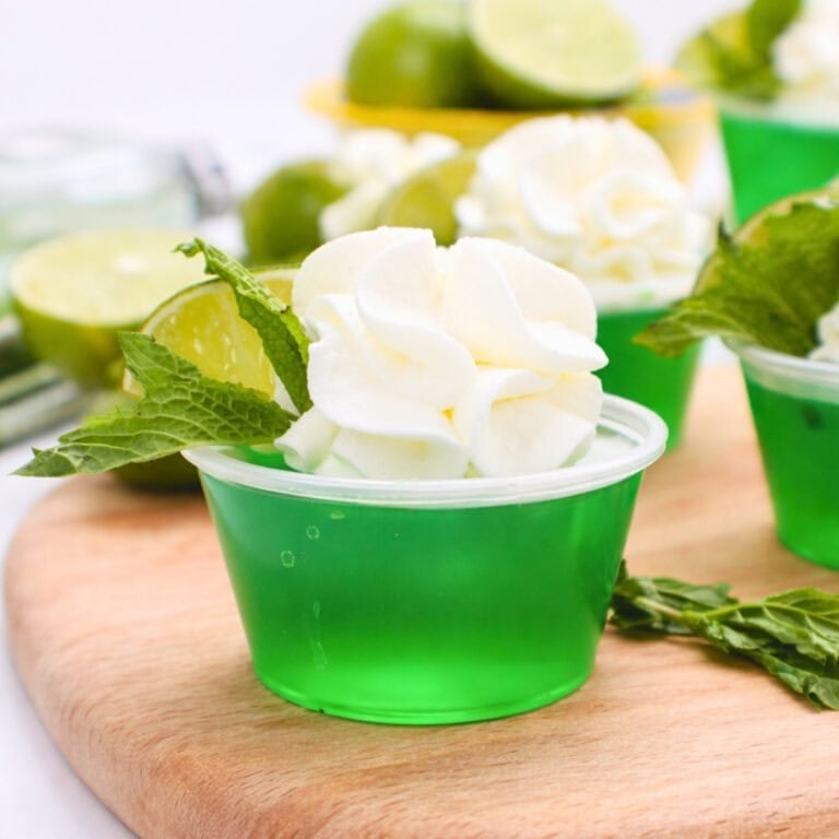 Green gelatin cup topped with whipped cream, a lime slice, and a mint sprig.