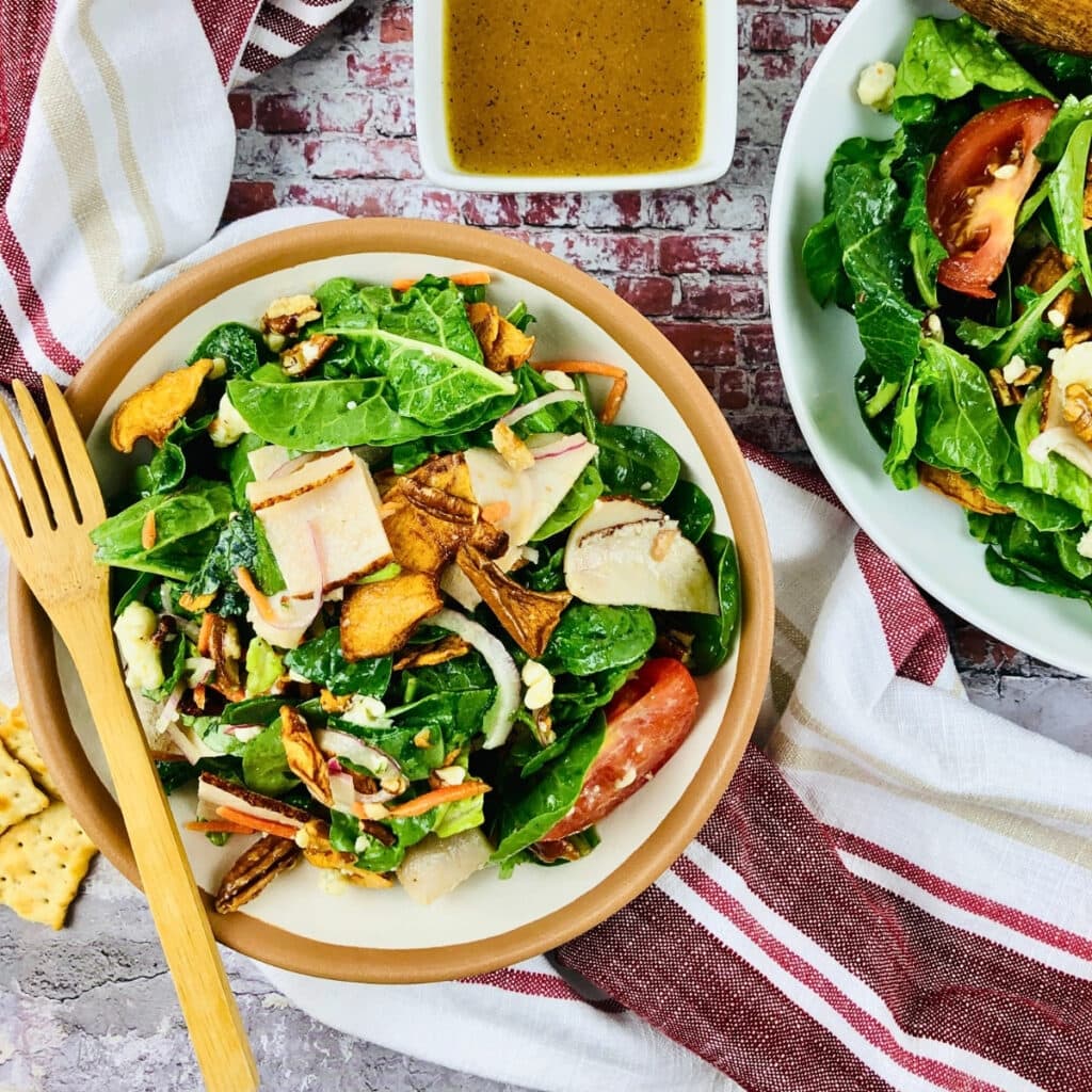 Two bowls of salad with greens, sliced tomatoes, and nuts, served with dressing.