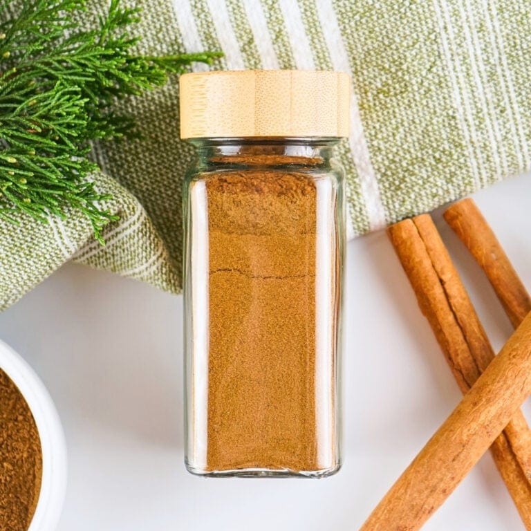 Square glass jar of ground cinnamon with a wooden lid.