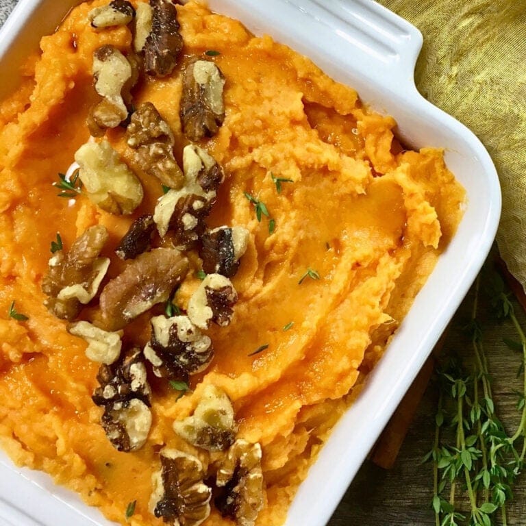 Mashed sweet potatoes topped with walnuts and fresh thyme in a white dish.