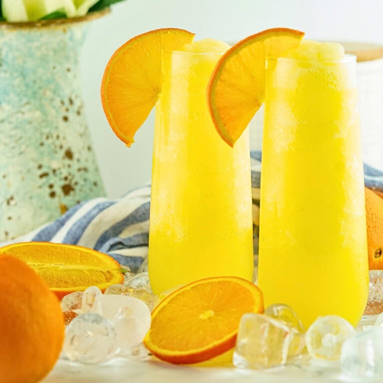 Two tall glasses of orange drink with orange slices and ice cubes nearby.
