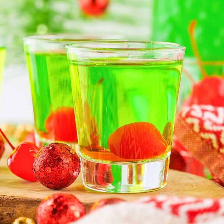Two shot glasses filled with green liquid and maraschino cherries.
