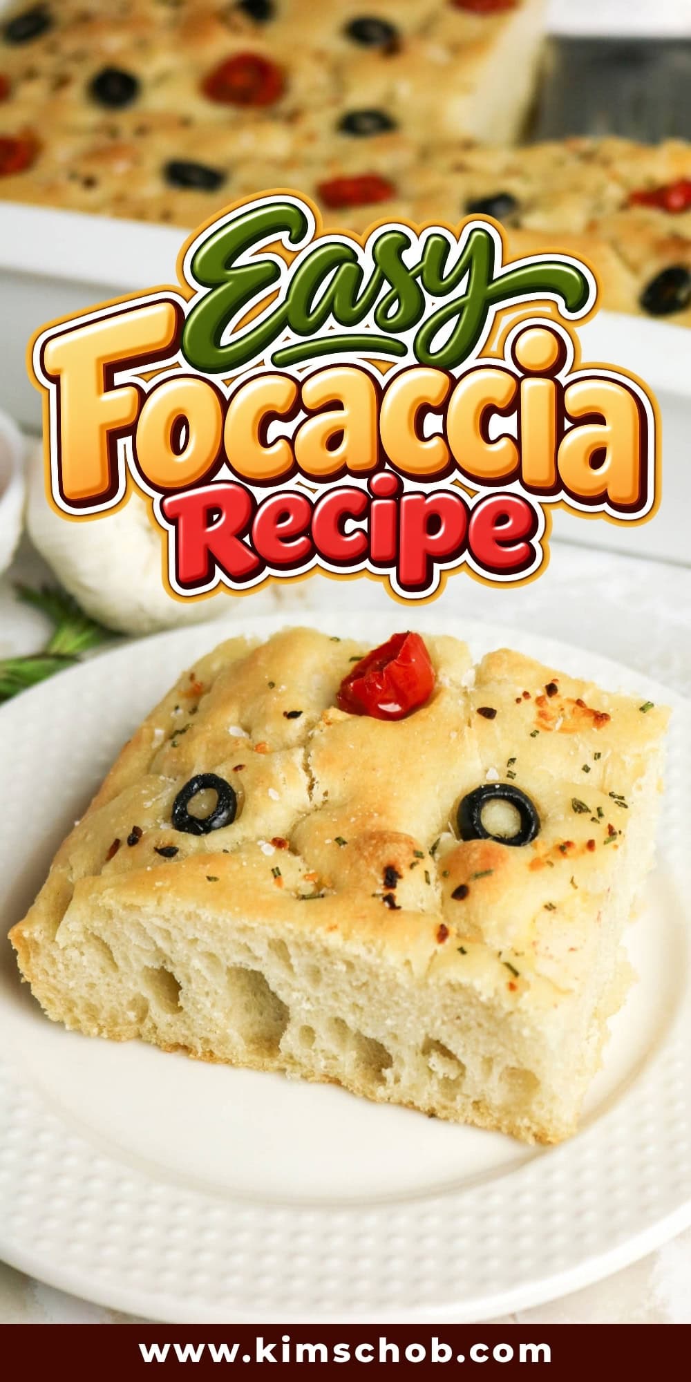 A square slice of focaccia with olives and a tomato on a white plate.