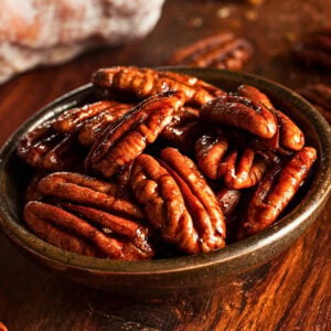 A ceramic bowl filled with glazed pecans.