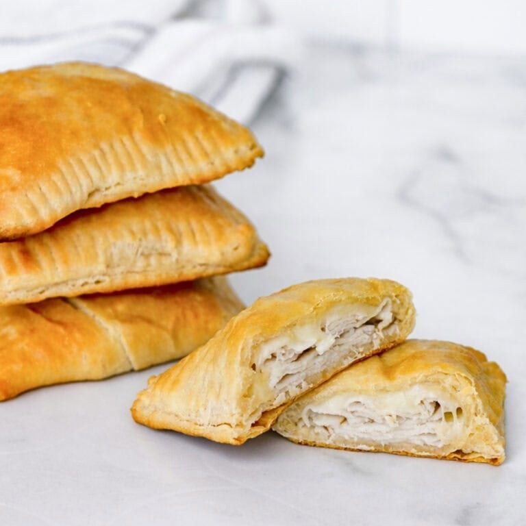 A stack of chicken and cheese hand pies, one cut open to show the filling.