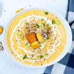 A bowl of creamy soup topped with croutons, scallions, and a swirl of cream.