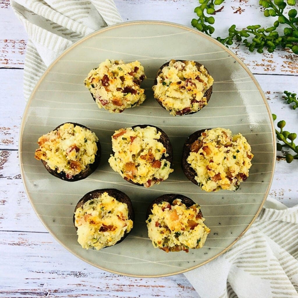 Seven stuffed mushrooms on a round plate with a striped napkin and greenery.