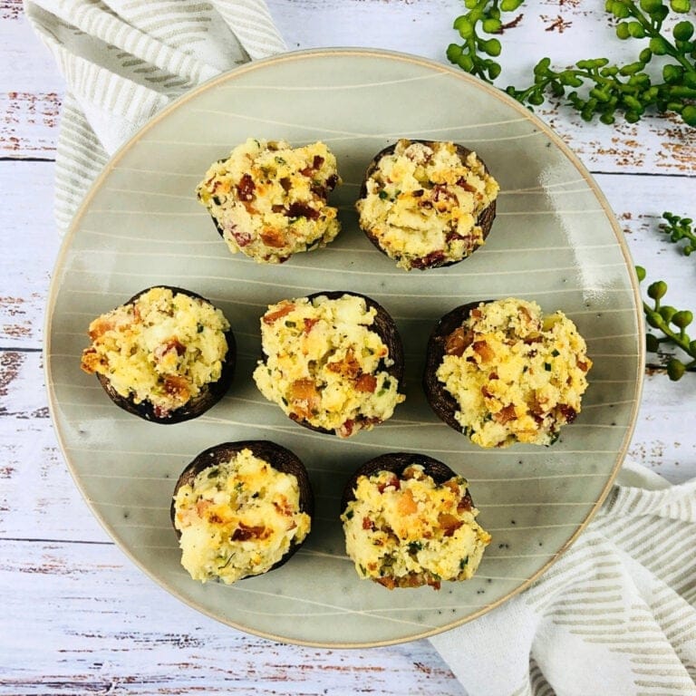 Seven stuffed mushrooms on a round plate with a striped napkin and greenery.
