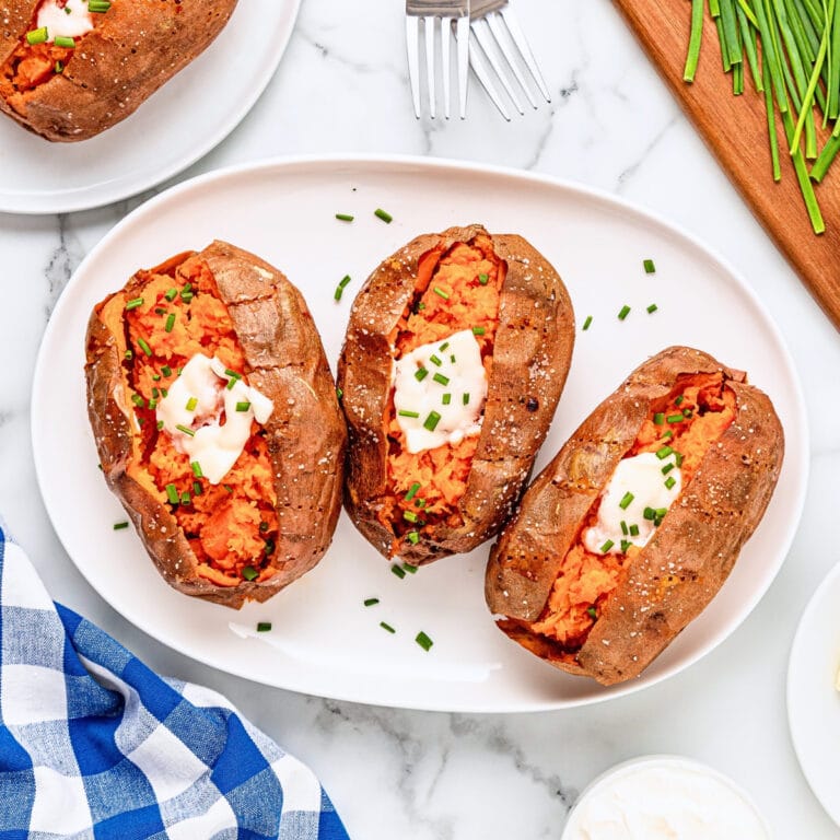 Three baked sweet potatoes topped with butter and chives on a white platter.