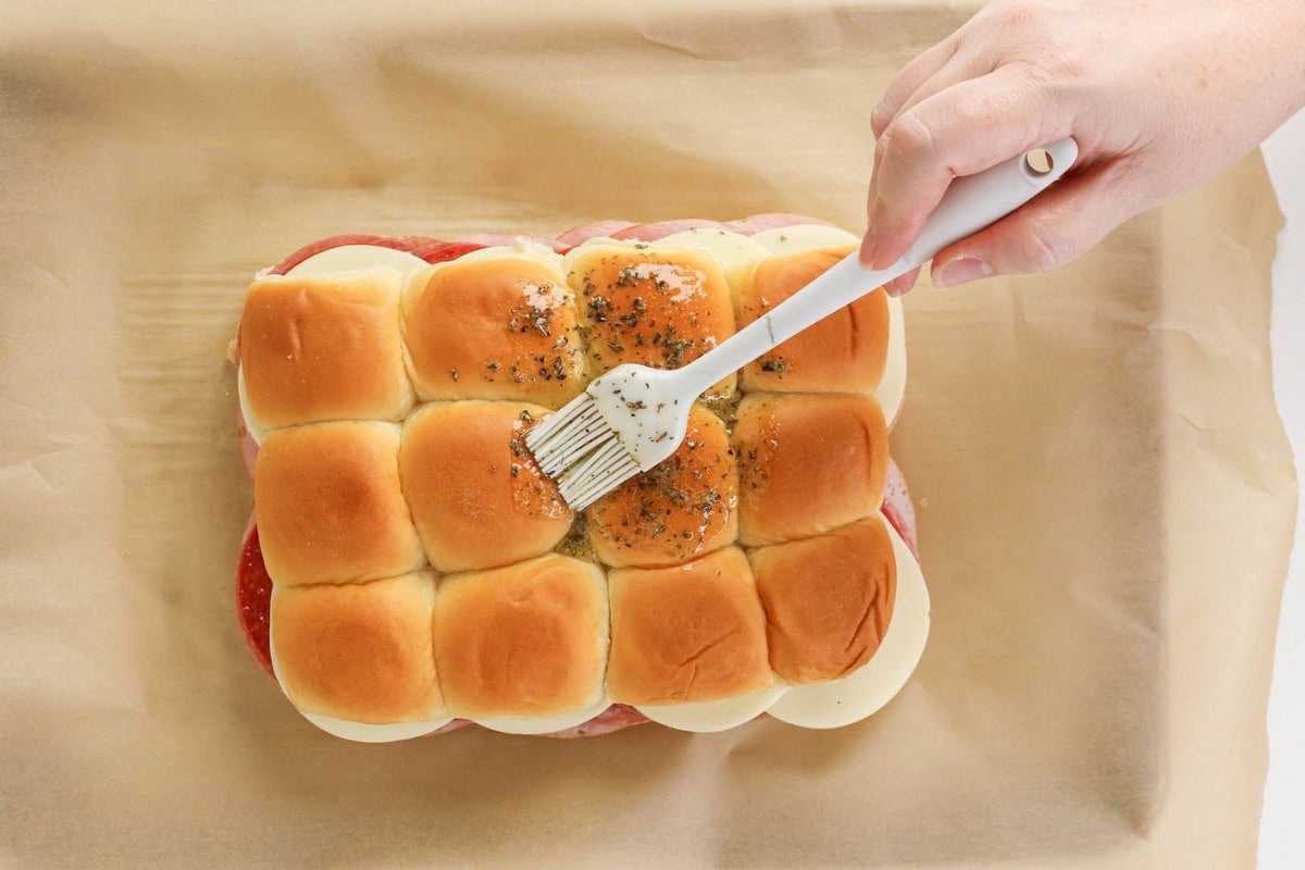 Hand brushing seasoning on top of a sandwich made with slider buns and cheese.