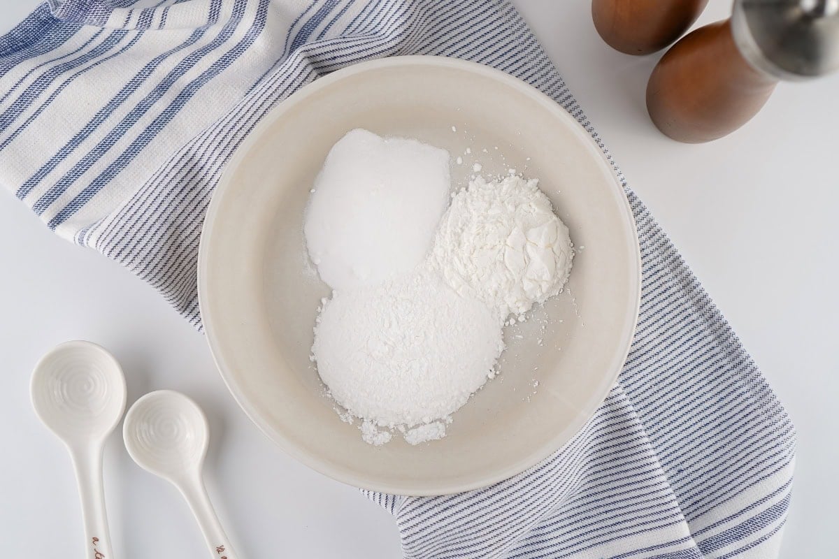A bowl containing three distinct piles of white baking ingredients.